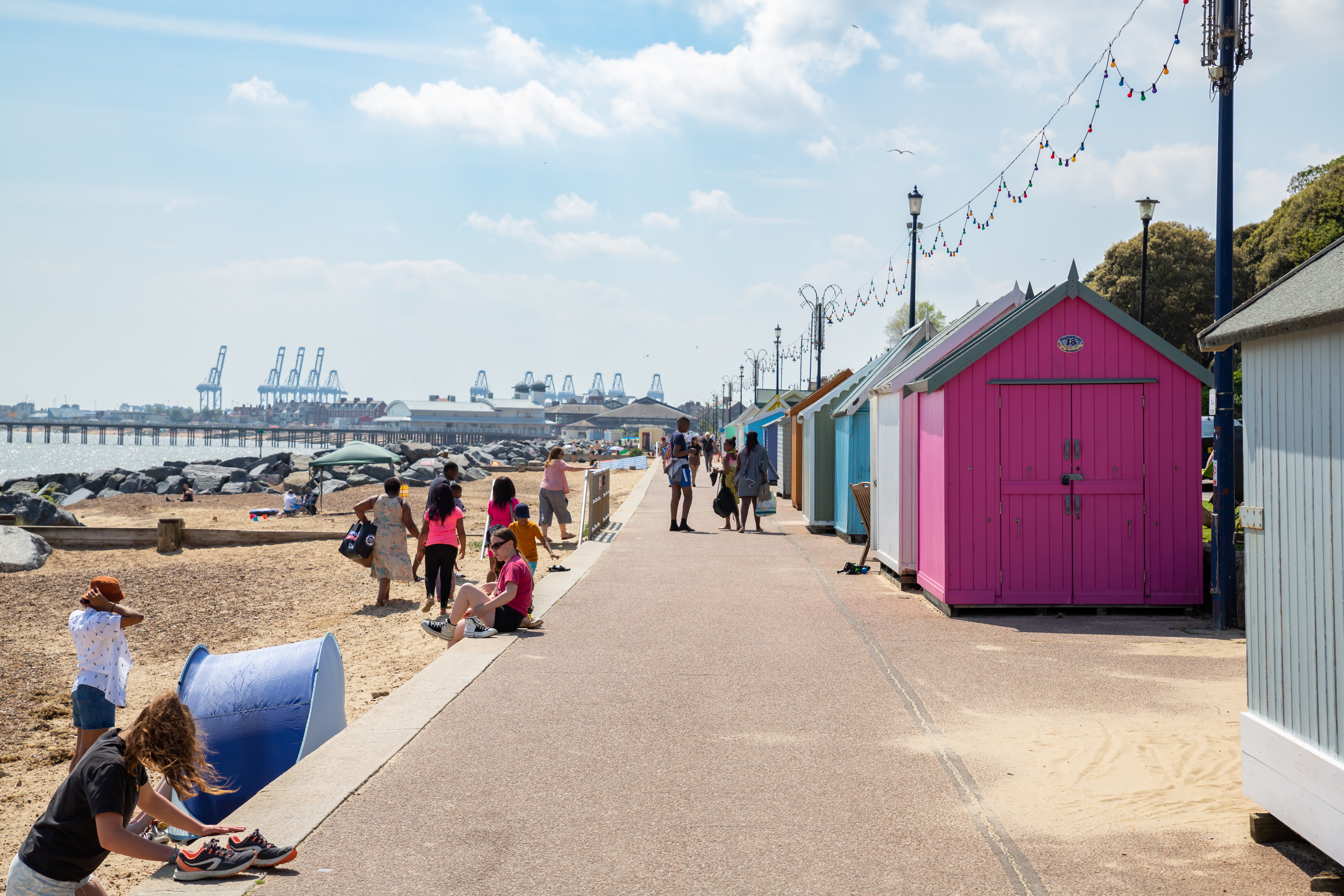Felixstowe seafront with people walking and colourful beach huts on a summer day